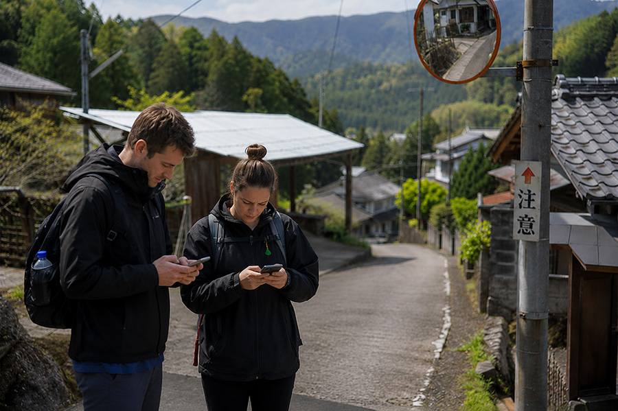 山あいの集落の坂道でスマートフォンの地図を確認する外国人旅行者のふたり